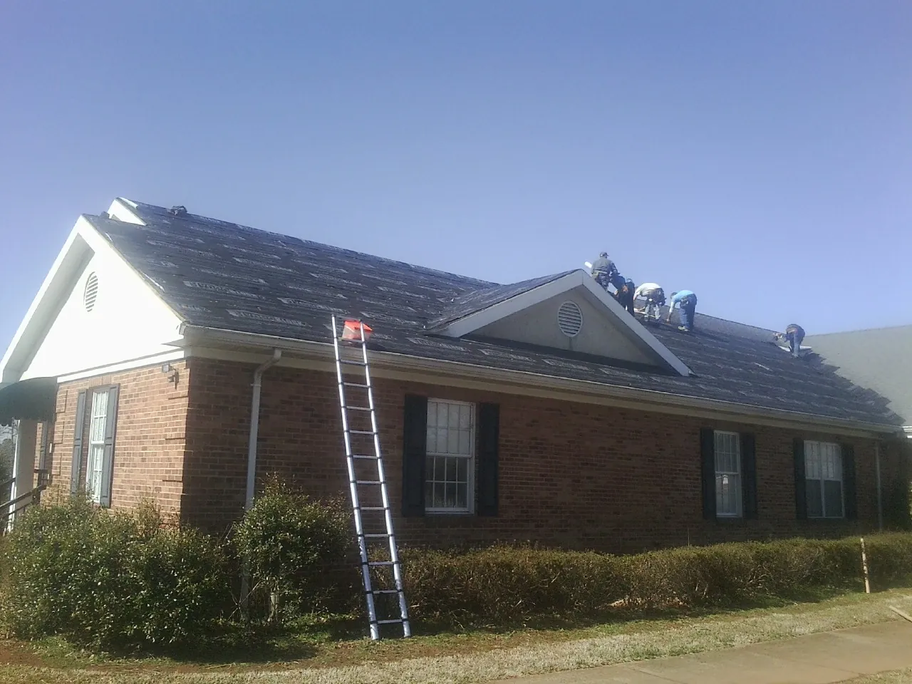 Crew tearing shingles off a brick ranch roof with a ladder set — Metal Roof Repair work by our crew in Brownstown