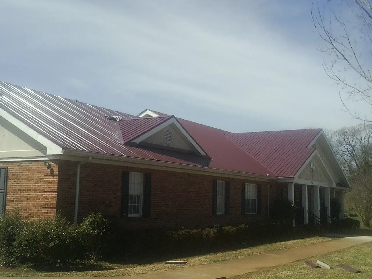 Red metal roof with gabled entries on a long brick building, from a Hail Damage Roof Repair job in Brownstown