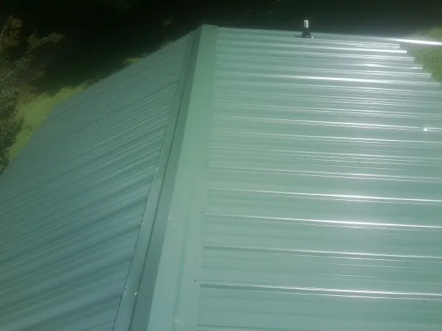 New green metal panels meeting at the ridge of a roof — Flat Roof Repair work by our crew in Brownstown