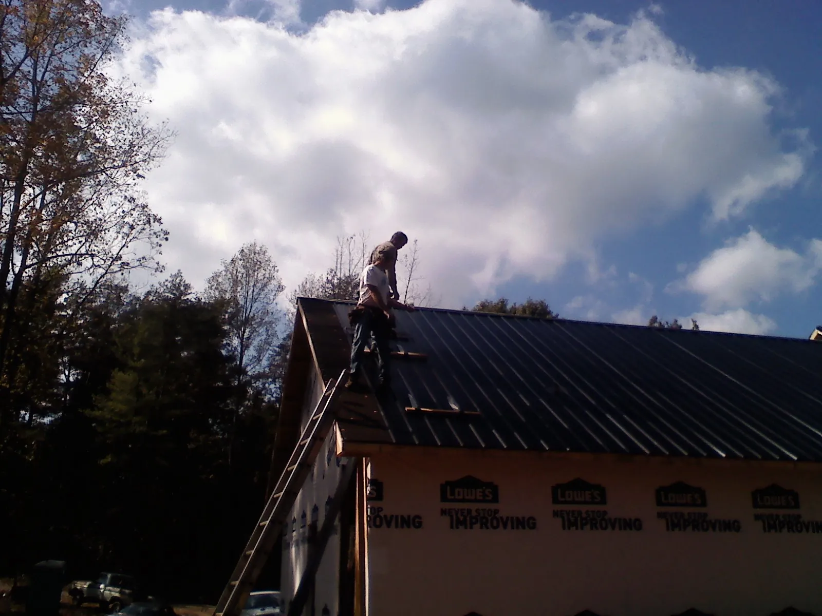 Roofer fastening dark metal panels high against a cloudy sky, from a Roof Inspection job in Brownstown