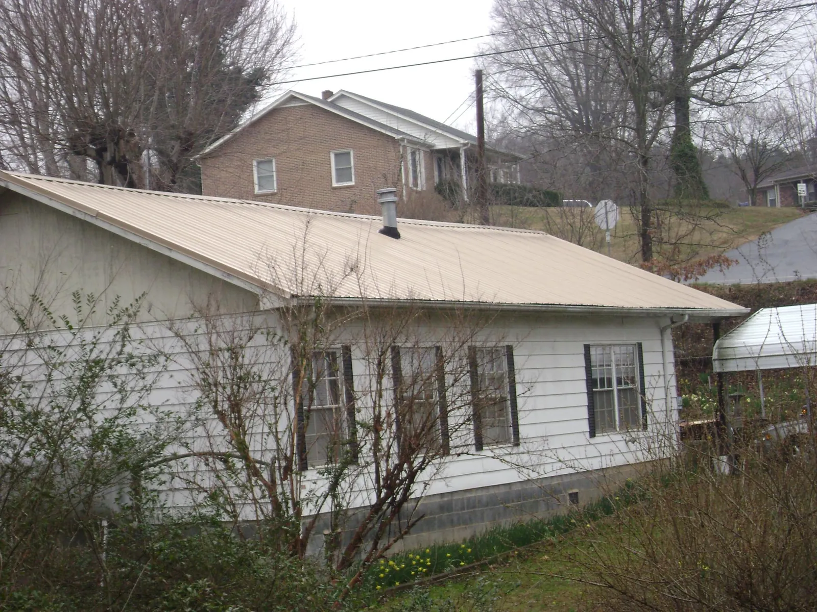 Tan metal roof on a white sided house set into a hillside — Commercial Roofing by Roofing Brothers in Brownstown