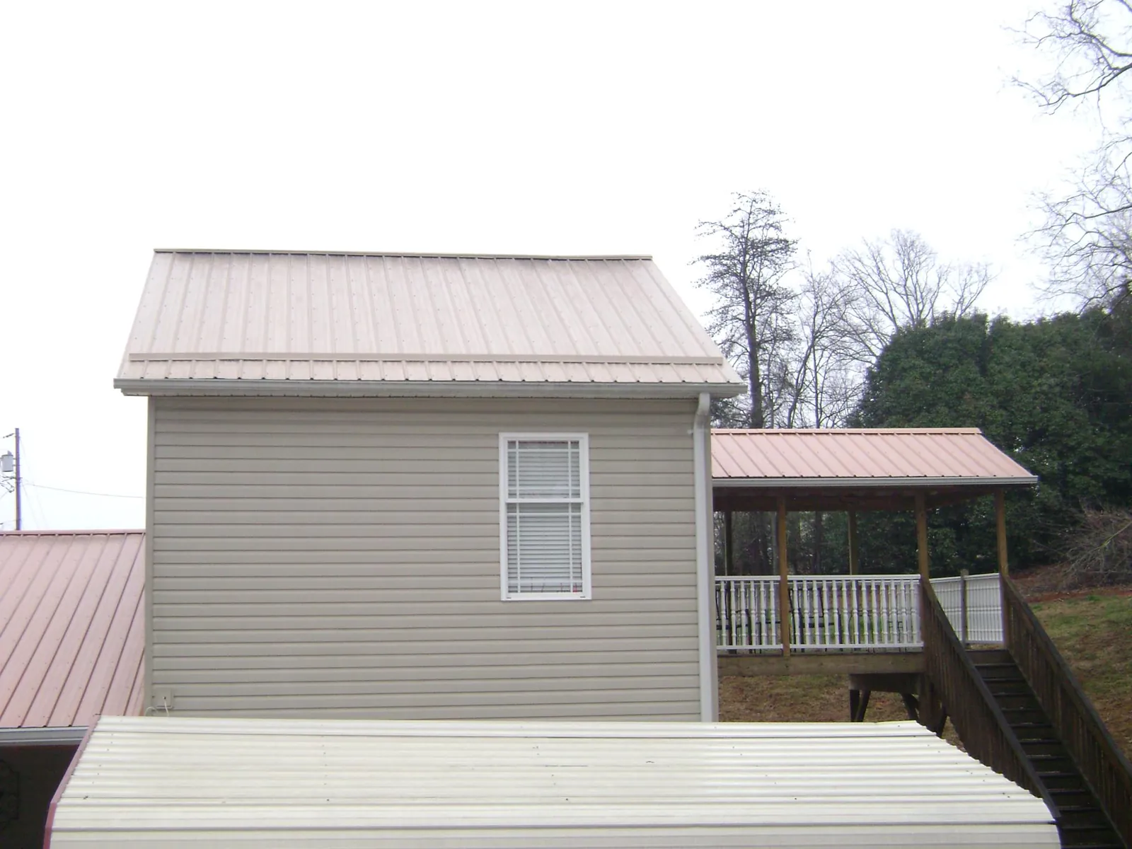 Tan metal roofs on a two story addition and attached porch, from a Roof Replacement job in Brownstown
